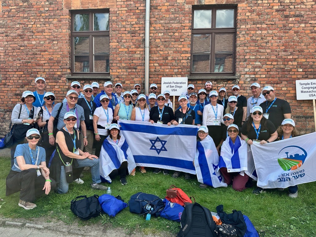 San Diego delegation sitting on grass and holding Israeli flag.