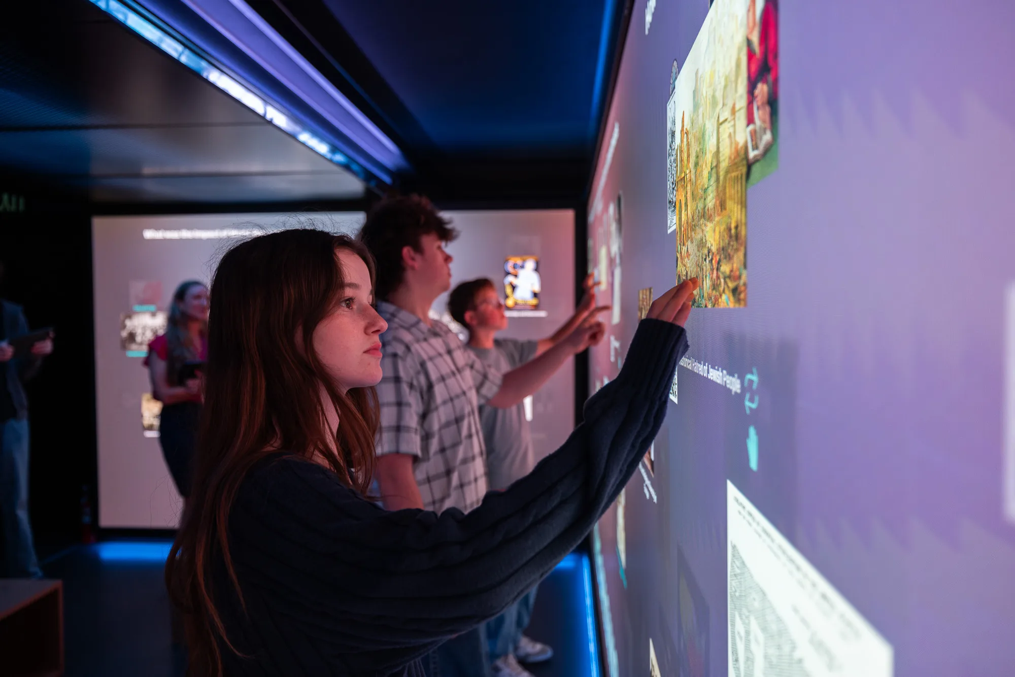 A student reaches for an interactive history wall inside Spark Interactive as classmates explore beside her