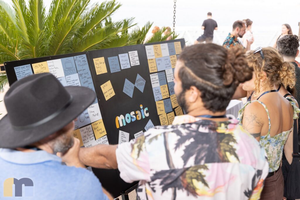 Members reading a board of sticky notes beneath the Mosaic wordmark at the launch on Shelter Island