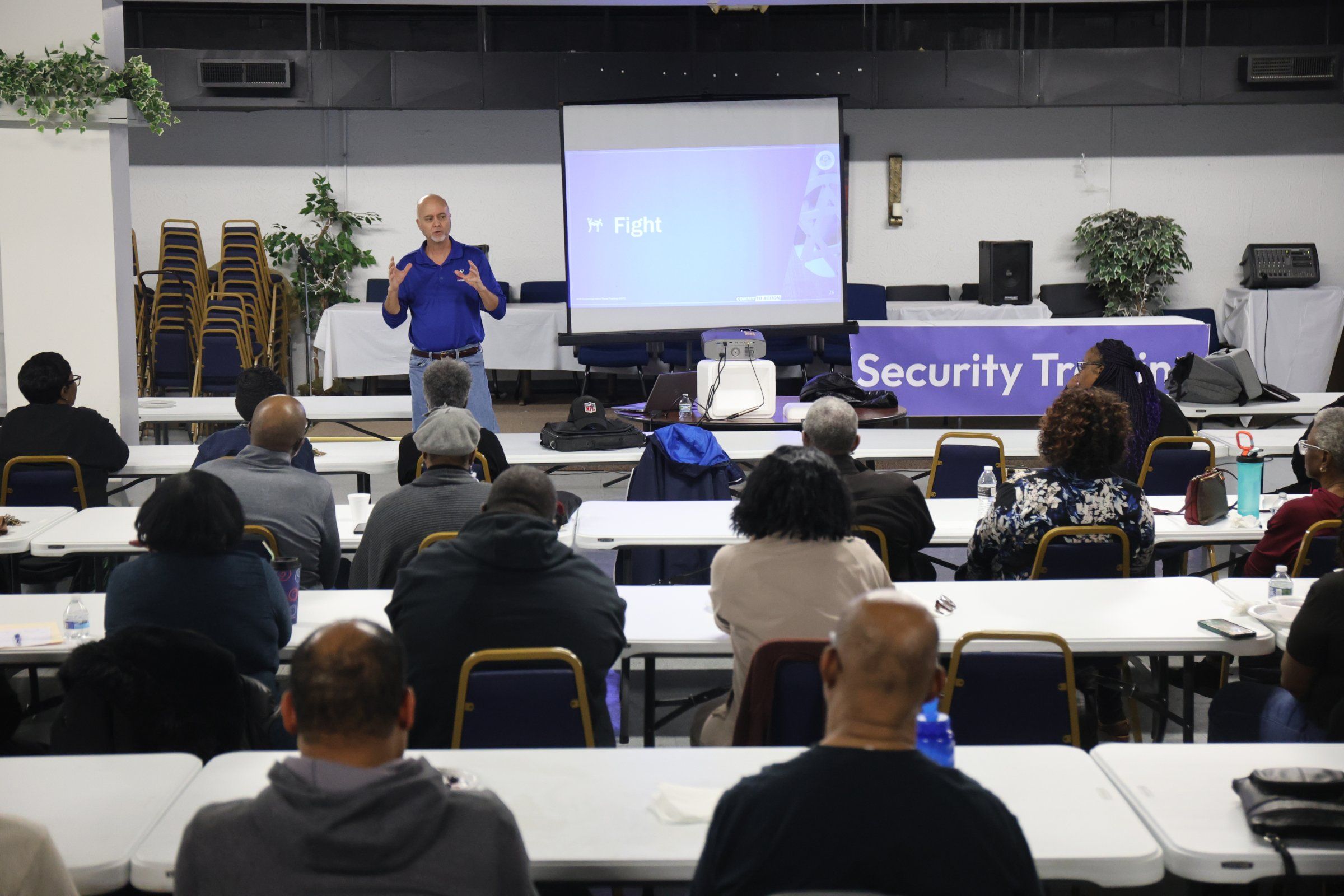 An instructor leads a room of community members through a security training session