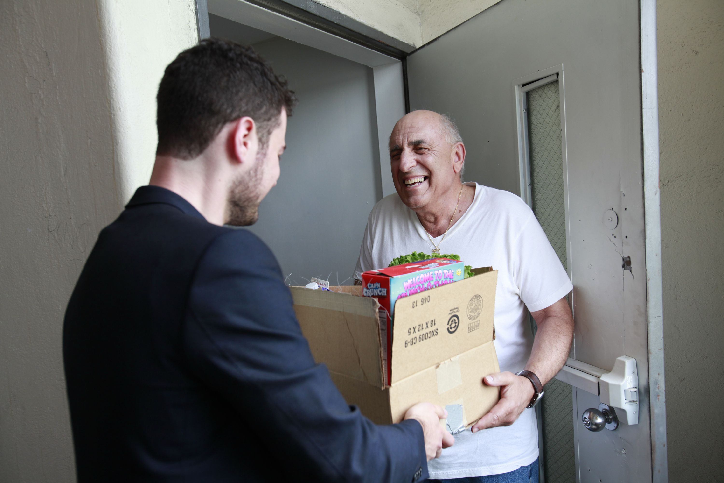 A volunteer delivering a box of food to an older man at his door