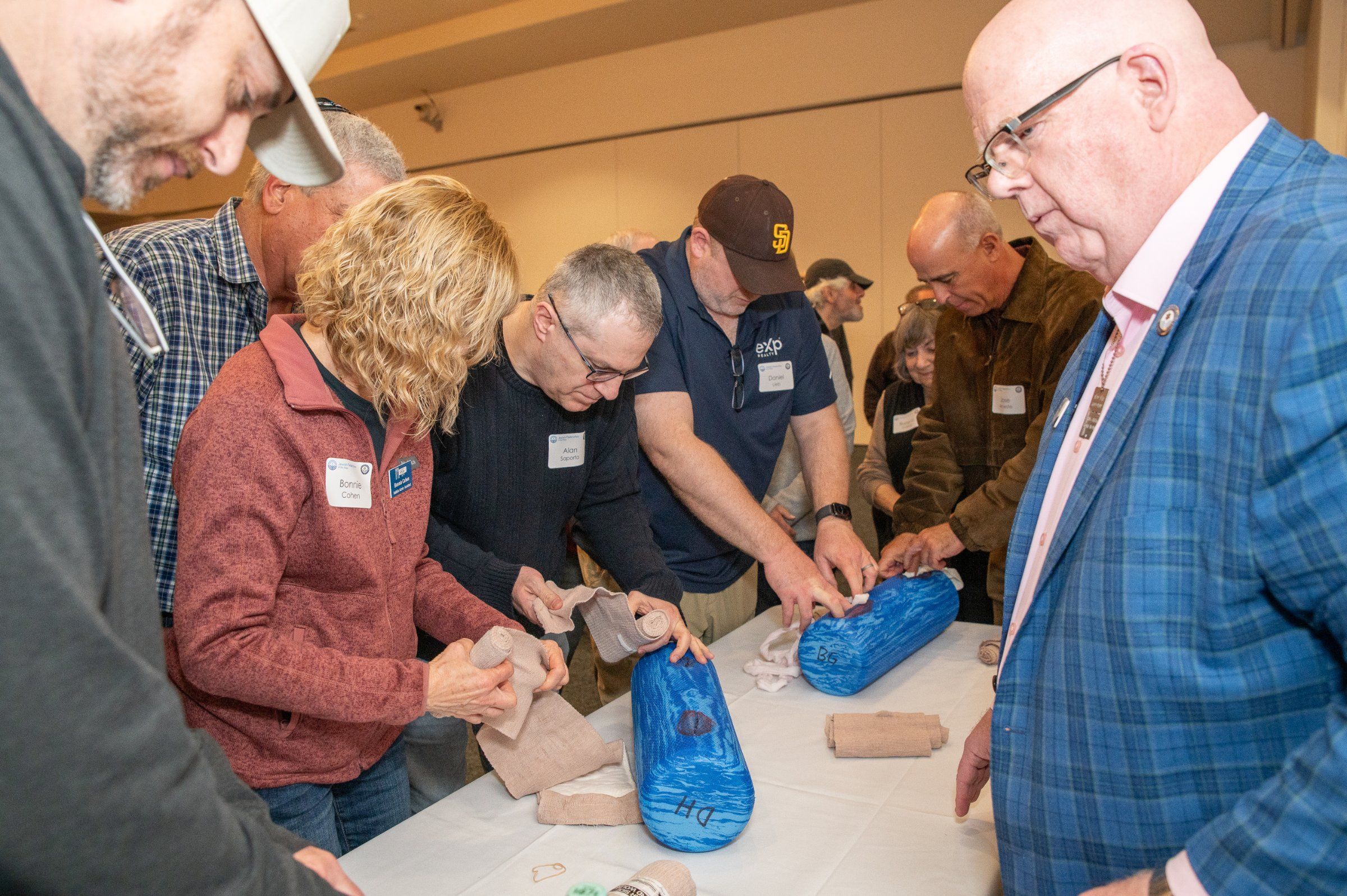 Community members pack wounds and wrap bandages on training aids while an instructor looks on